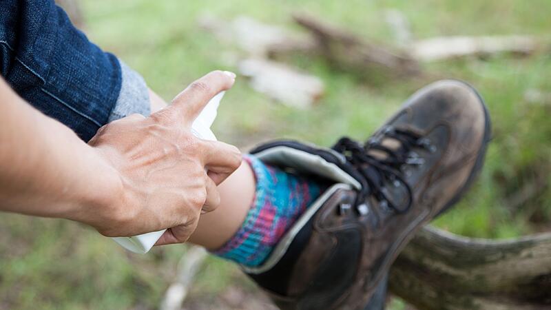 Frau sprüht Waden mit einem Insektenschutzmittel ein