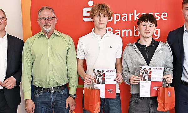 Vorstandsvorsitzender Stephan Kirchner (links) und Wertpapierbeauftragter David Förtsch (rechts) gratulieren Samuel Ziegelhöfer und Leon Motschenbacher vom Siegerteam „Gejagt vom Finanzamt“ vom Clavius-Gymnasium, zusammen mit ihrem Lehrer Jürgen S...