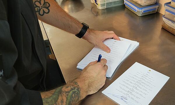 Dominik Käppeler unterschreibt die Menüs, die die Gäste erst am Ende des Abends erhalten. Auf dem linken Unterarm ist der Michelin-Stern als Tattoo zu sehen.