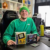 Ganz in grün: Jonas Steinbeißer alias der Fustler sitzt in seinem Streamingzimmer. Vor ihm stehen zwei seiner Lieblingssammelstücke: ein originaler Gameboy-Colour und ein Videospiel.