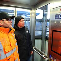 Jürgen Hälter (l.) vom Bahnhofsmanagement Nordfranken und Bürgermeister Mario Schönwald fahren mit dem Aufzug nach unten.