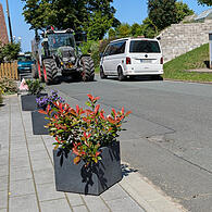 Damit bei Gegenverkehr keine Fahrzeuge über private Hofflächen ausweichen, hilft man sich in Greiendorf mit dicken Holzklötzen oder (wie hier im Bild) mit Blumenkübeln.