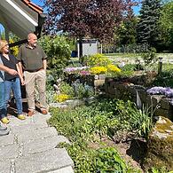 Kreisfachberater Guntram Ulsamer mit Heidi und Rainer Ledermann vor ihrer Terrasse mit Sandsteinmauern und blühendem Steingarten.