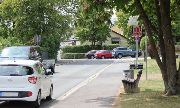 Geschwindigkeitsanzeigen sollen vor der Grundschule den Verkehr verlangsamen. Einige Autos bremsen ab, bis der Smiley grün lacht. Andere nicht.