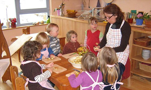 Im Waldorfkindergarten Wernstein schneiden Kinder mit Einrichtungsleiterin Elfriede Sauer Äpfel für einen Kuchen.