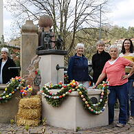 Die Frauen vom Heimat- und Wanderverein Aschach stehen vor dem geschmückten Osterbrunnen