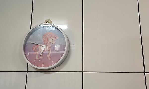 Die pinke Einhorn-Uhr hängt an der Wand über dem Herd und hebt sich von der weißen Fliesenwand ab.