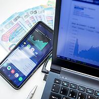 Smartphone, Laptop und Geldscheine auf einem Schreibtisch