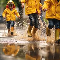 Kinder spielen mit Gummistiefeln im Regen
